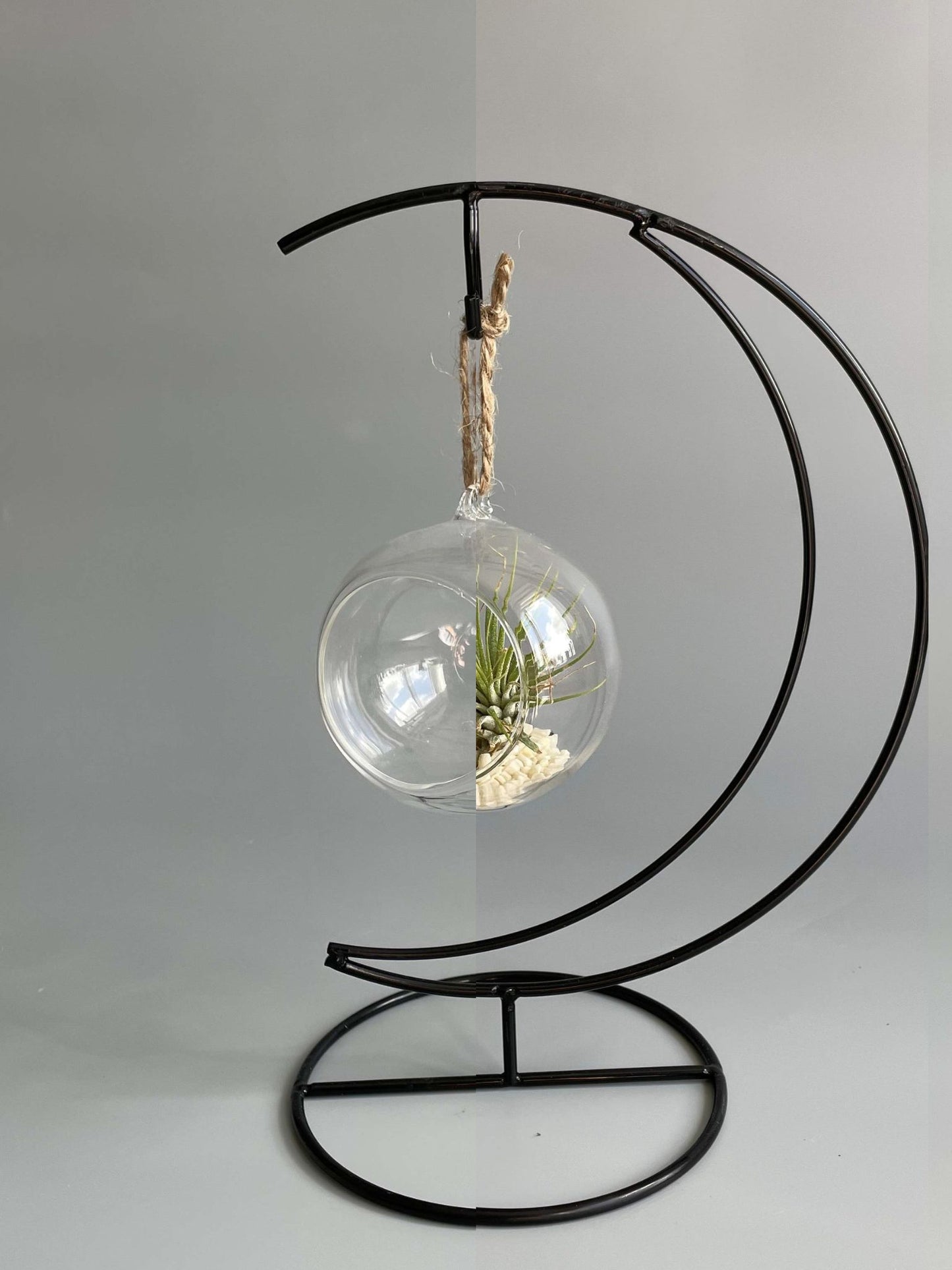 Decorative hanging plant holder with glass sphere and metal crescent moon stand on a plain background